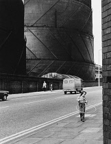 England, Merseyside, Bootle, Seventies street scene with young girl playing Hula Hoop and gasometer in the background.