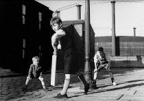 England, Merseyside, Kirkdale, Children playing cricket on cobbled street, using lampost as wicket.