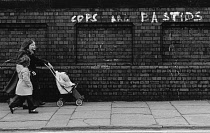 England, Merseyside, Liverpool, Graffiti with Cops are Bastids written on brick wall as children walk by, 1972.