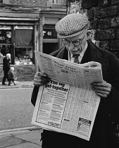 England, Merseyside, Bootle, Elderly man with flat cap and glasses reading the Daily Mail newspaper 1st May 1971.