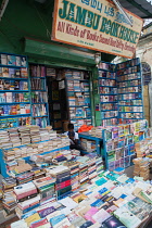 India, Pondicherry, Second-hand bookshop in market with seller using ebook or tablet computer.