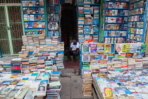 India, Pondicherry, Second-hand bookshop in market with seller using ebook or tablet computer.