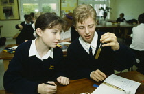 Education, Science Class, Two students in uniform at desk examining contents of test tube with open exercise books, pens and pencils in front of them.