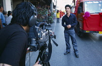 Thailand, North, Chiang Mai, Man with professional video camera aimed at man standing by the road.