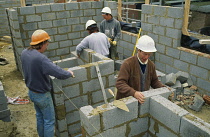 Architecture, Construction, Men working on building site wearing hard hats laying courses of concrete blocks.