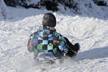 England, Young person sledding down hill in snow.