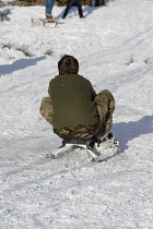 England, Young person tobogganing down hill in snow.