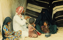 Qatar, General, Bedouin family in tent entrance with woman wearing black dress and head dress covering all her face except for her eyes.