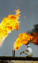 Qatar, General, Man squating on the ground with gas flares in the distance.