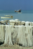 Qatar, Ruwais, Fishing nets drying by the sea with fishing dhows at anchor beyond.
