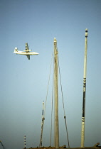 Qatar, Doha, Airplane in the sky with dhow masts in the foreground.