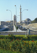 Qatar, Doha, Mans watering  public plants with minaret behind.