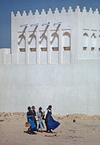 Qatar, Doha, Young schoolgirls walking past traditional building.