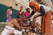 India, Uttar Pradesh, Varanasi, A saddhu performs a puja for a bereaved family on the ghats.