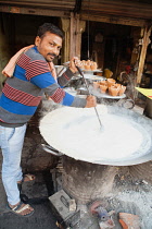 India, Uttar Pradesh, Allahabad, A vendor stirs a large pan of mishti doi sweet curd at a food hotel.