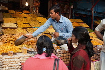 India, Uttar Pradesh, Lucknow, A vendor serves customers at his namkeen & savoury snacks stall.