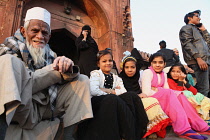 India, New Delhi, Muslim girls & their grandfather sit on the steps in front of the entrance to the Jama Masjid in the old city of Delhi.