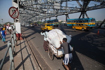 India, West Bengal, Kolkata, Men push a cart loaded with goods across Howrah Bridge.