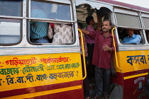 India, West Bengal, Kolkata, A bus conductor stands in the foot well of a public bus.