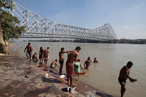 India, West Bengal, Kolkata, Men wash and bathe in the Hooghly River with Howrah Bridge in the background.
