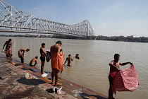 India, West Bengal, Kolkata, Men wash and bathe in the Hooghly River with Howrah Bridge in the background.