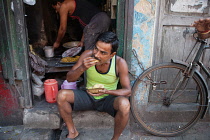 India, West Bengal, Kolkata, A man eating a snack of pani puri and vegetables.