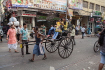 India, West Bengal, Kolkata, A rickshaw driver pulls passengers through the streets of the Bara Bazar district.