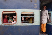 India, West Bengal, Asansol, Passengers at the window & footplate of a train carriage at railway station.