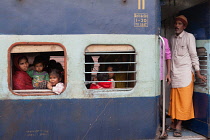 India, West Bengal, Asansol, Passengers at the window & footplate of a train carriage at railway station.