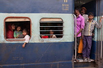 India, West Bengal, Asansol, Passengers at the window & footplate of a train carriage at railway station.