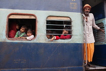 India, West Bengal, Asansol, Passengers at the window & footplate of a train carriage at railway station.