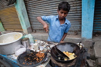 India, West Bengal, Asansol, A boy fries chilli pakora on a street food cart.