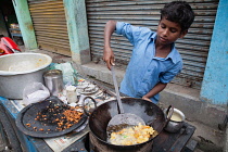 India, West Bengal, Asansol, A boy fries chilli pakora on a street food cart.