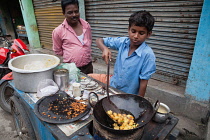 India, West Bengal, Asansol, A boy fries chilli pakora on a street food cart.