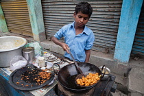 India, West Bengal, Asansol, A boy fries chilli pakora on a street food cart.