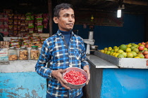 India, West Bengal, Asansol, Portrait of a juice vendor holding a bowl of pomegranate seeds.