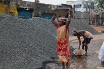 India, West Bengal, Asansol, A female labourer carrying a container of stone chippings on her head.