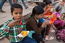 India, Uttar Pradesh, Varanasi, Children eat a snack of bhel puri on the ghats.