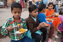 India, Uttar Pradesh, Varanasi, Children eat a snack of bhel puri on the ghats.