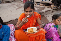 India, Uttar Pradesh, Varanasi, A woman eats a snack of bhel puri & kachori on the ghats.