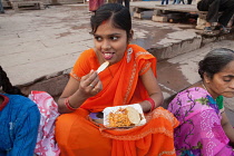 India, Uttar Pradesh, Varanasi, A woman eats a snack of bhel puri & kachori on the ghats.