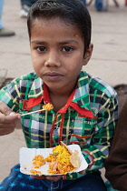 India, Uttar Pradesh, Varanasi, A boy eats a snack of bhel puri on the ghats.