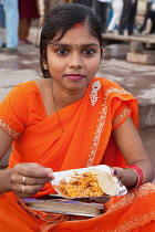 India, Uttar Pradesh, Varanasi, A woman eats a snack of bhel puri & kachori on the ghats.