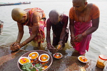 India, Uttar Pradesh, Varanasi, Female pilgrims pray and make offerings at the River Ganges.