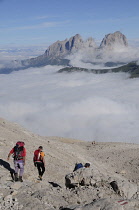 Italy, Trentino Alto Adige, Marmolada, view across to Sasso Lungo mountain range with 2 hikers.