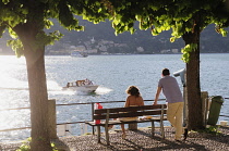 Italy, Lombardy, Lake Como, Bellagio, couple on bench at sunset.