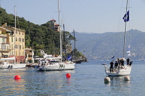 Italy, Liguria, Portofino, waterside houses with sailing boat leaving the bay.