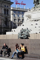 Italy, Lombardy, Milan, Piazza Duomo, sitting at the foot of monument to Vittorio Emanuele II.