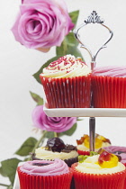 Studio shot of colourfully decorated cupcakes on cake stand with pink roses behind.