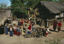 Thailand, Karen Village, People gathered by log pile outside thatched houses.
